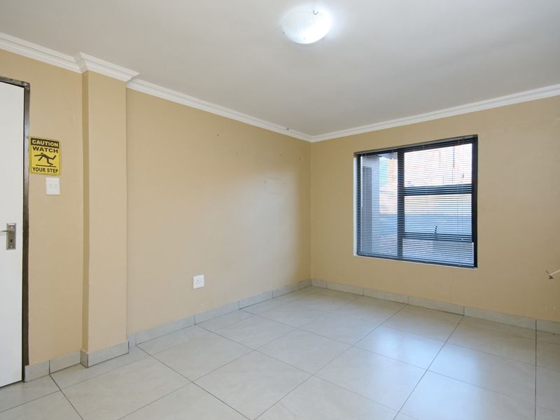 An empty bedroom featuring neutral wall paint, tiled flooring, and an aluminium window with fitted blinds.