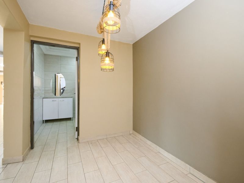 A clean, neutral-toned hallway featuring modern pendant lighting and tiled flooring, with a direct view into an adjacent bathroom with a vanity unit.