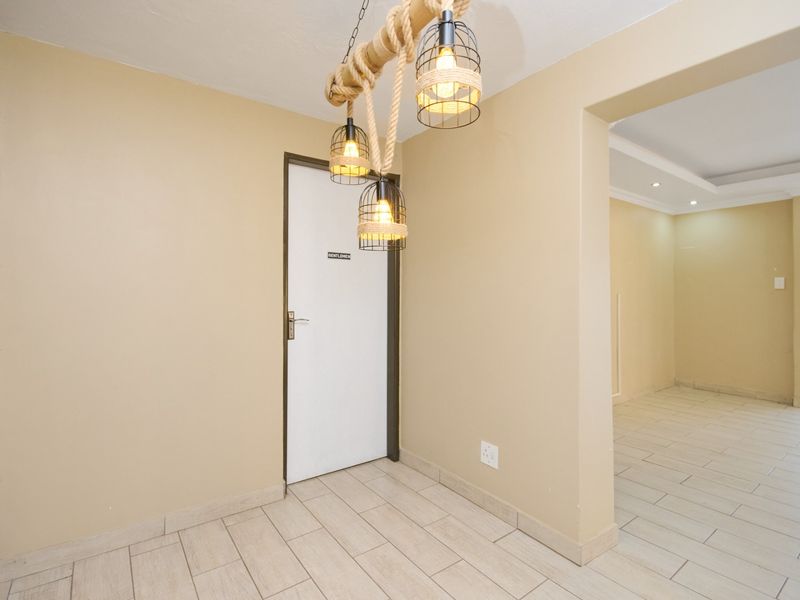 A clean, neutral-toned hallway featuring tiled flooring and a doorway leading into an adjacent living space.