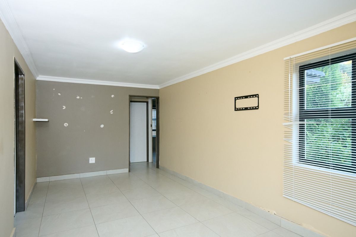 An empty living room featuring tiled flooring, neutral wall tones, and a window with fitted blinds, requiring minor cosmetic repairs to walls.