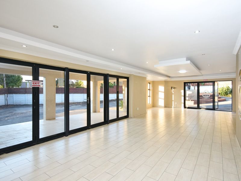 Spacious open-plan area featuring neutral tiled flooring, recessed ceiling lighting, and large black aluminium sliding doors providing access to the exterior.