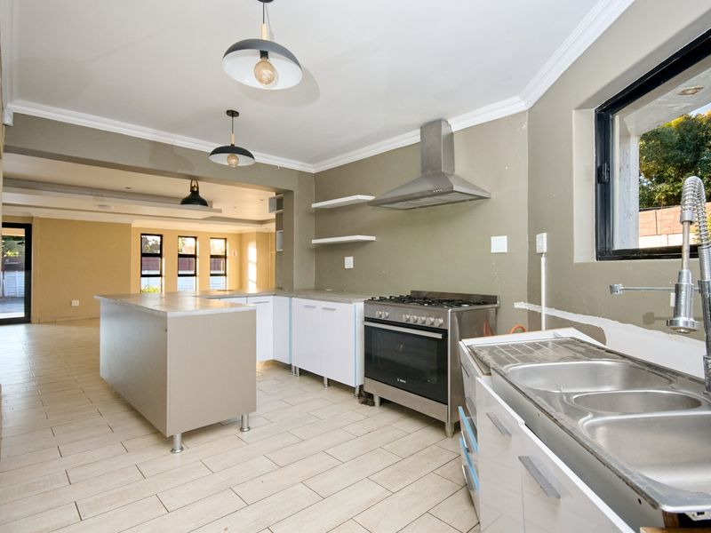 Modern open-plan kitchen featuring a central island, stainless steel gas stove, extractor fan, and double bowl sink with tiled flooring throughout.
