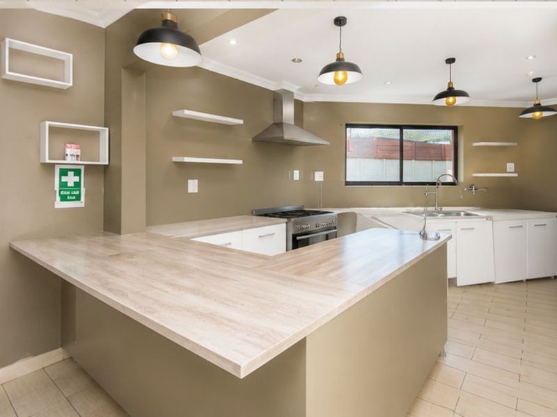 A clean, modern kitchen featuring laminate countertops, a gas stove, stainless steel extractor fan, and ample built-in cabinetry with contemporary pendant lighting.