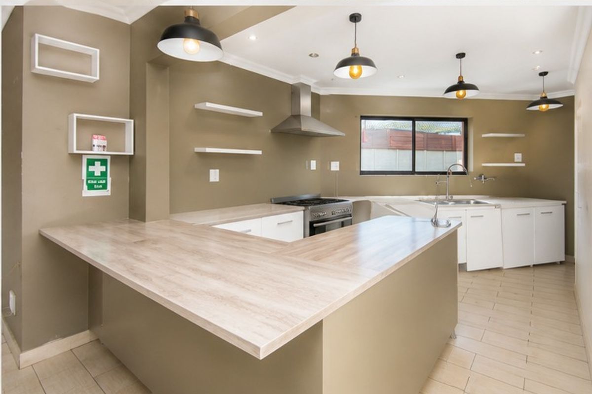 A clean, modern kitchen featuring laminate countertops, a gas stove, stainless steel extractor fan, and ample built-in cabinetry with contemporary pendant lighting.