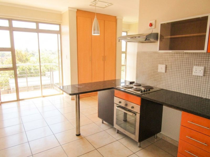 Open-plan kitchen featuring granite countertops, built-in oven and hob, and tiled flooring, with direct access to a balcony through sliding glass doors.