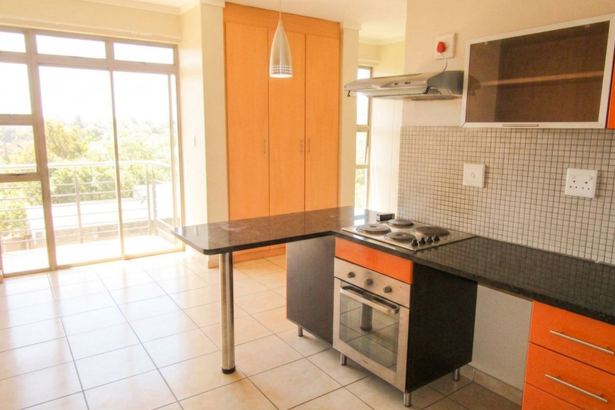 Open-plan kitchen featuring granite countertops, built-in oven and hob, and tiled flooring, with direct access to a balcony through sliding glass doors.