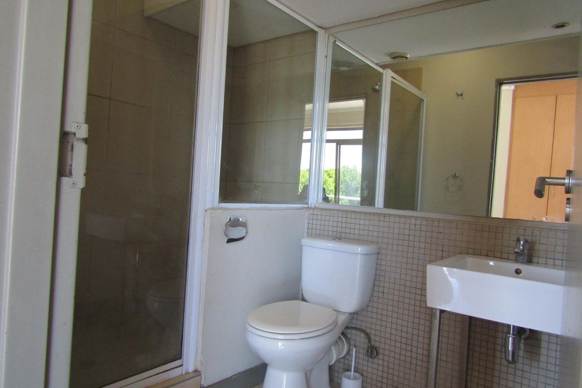 A functional bathroom featuring a shower enclosure, pedestal washbasin, and wall-mounted mirror with tiled splashback finishes.