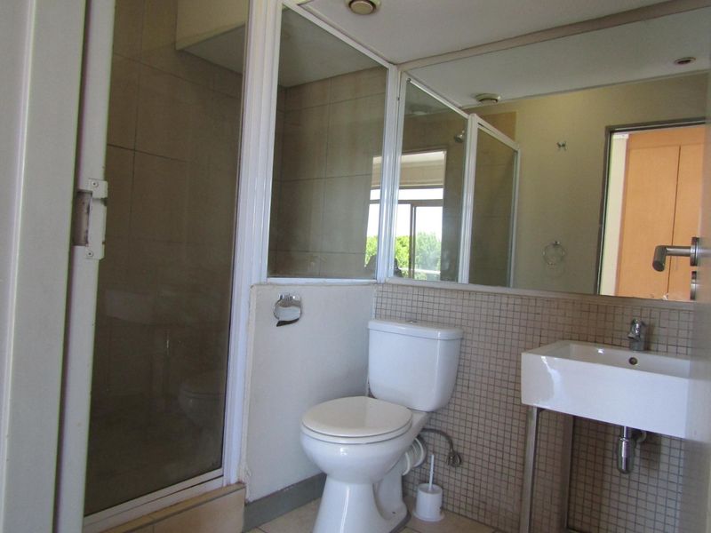 A functional bathroom featuring a shower enclosure, pedestal washbasin, and wall-mounted mirror with tiled splashback finishes.