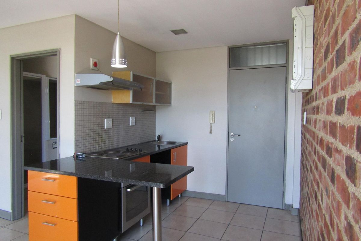 Compact kitchen featuring orange cabinetry, granite countertops, built-in oven and hob, and an exposed brick feature wall.