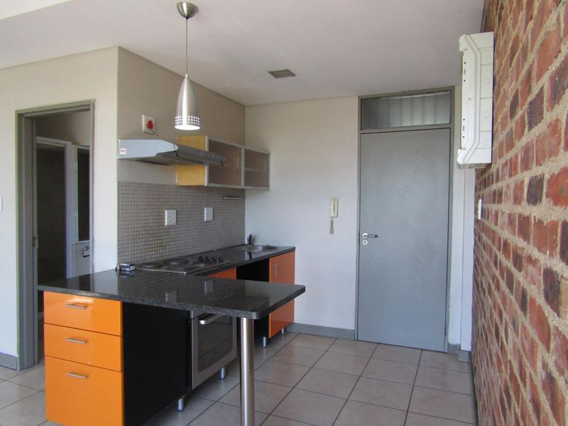 Compact kitchen featuring orange cabinetry, granite countertops, built-in oven and hob, and an exposed brick feature wall.