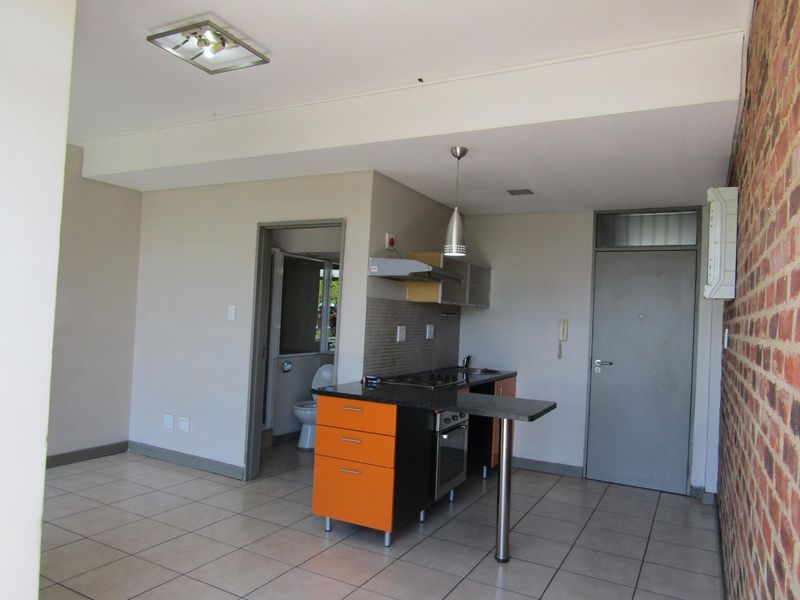 Open plan living area featuring a compact kitchen with built-in oven, hob, extractor fan, and an exposed brick feature wall with tiled flooring throughout.