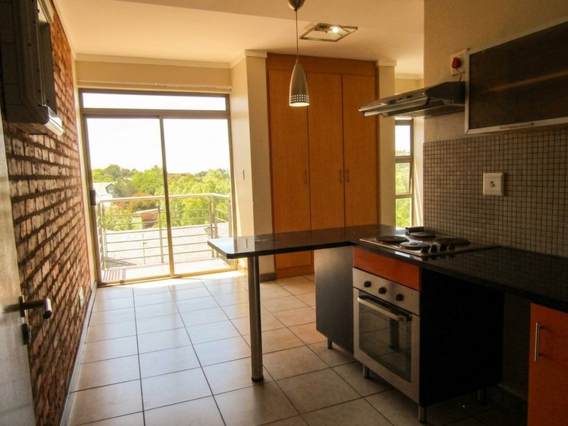 Open-plan kitchen and living area featuring exposed brick walls, tiled flooring, built-in cabinetry, and a breakfast bar with access to a balcony.