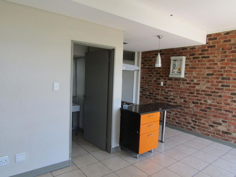 A compact kitchen area featuring an exposed brick wall, tiled flooring, and a built-in island with a granite countertop.