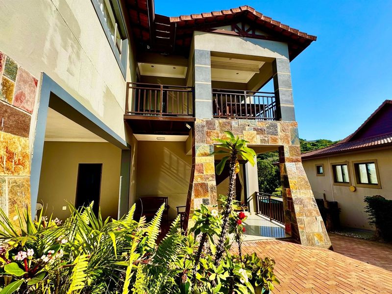 Rear view of the property featuring a multi-level design with stone-clad pillars, a covered patio, and an upper-level balcony with metal railings.