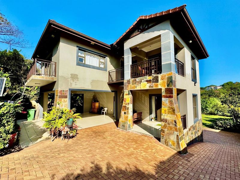 A multi-story residential property featuring stone cladding accents, a tiled roof, a paved driveway, and multiple balconies overlooking the surrounding landscape.
