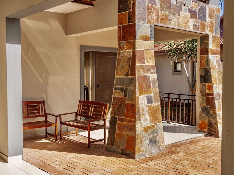 A covered patio area featuring a distinctive stone-clad pillar and brick paving, providing a pleasant outdoor space for relaxation.
