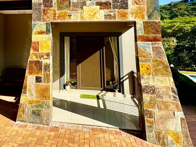 Front entrance featuring decorative stone cladding, a tiled porch area, and a modern sliding glass door leading into the home.
