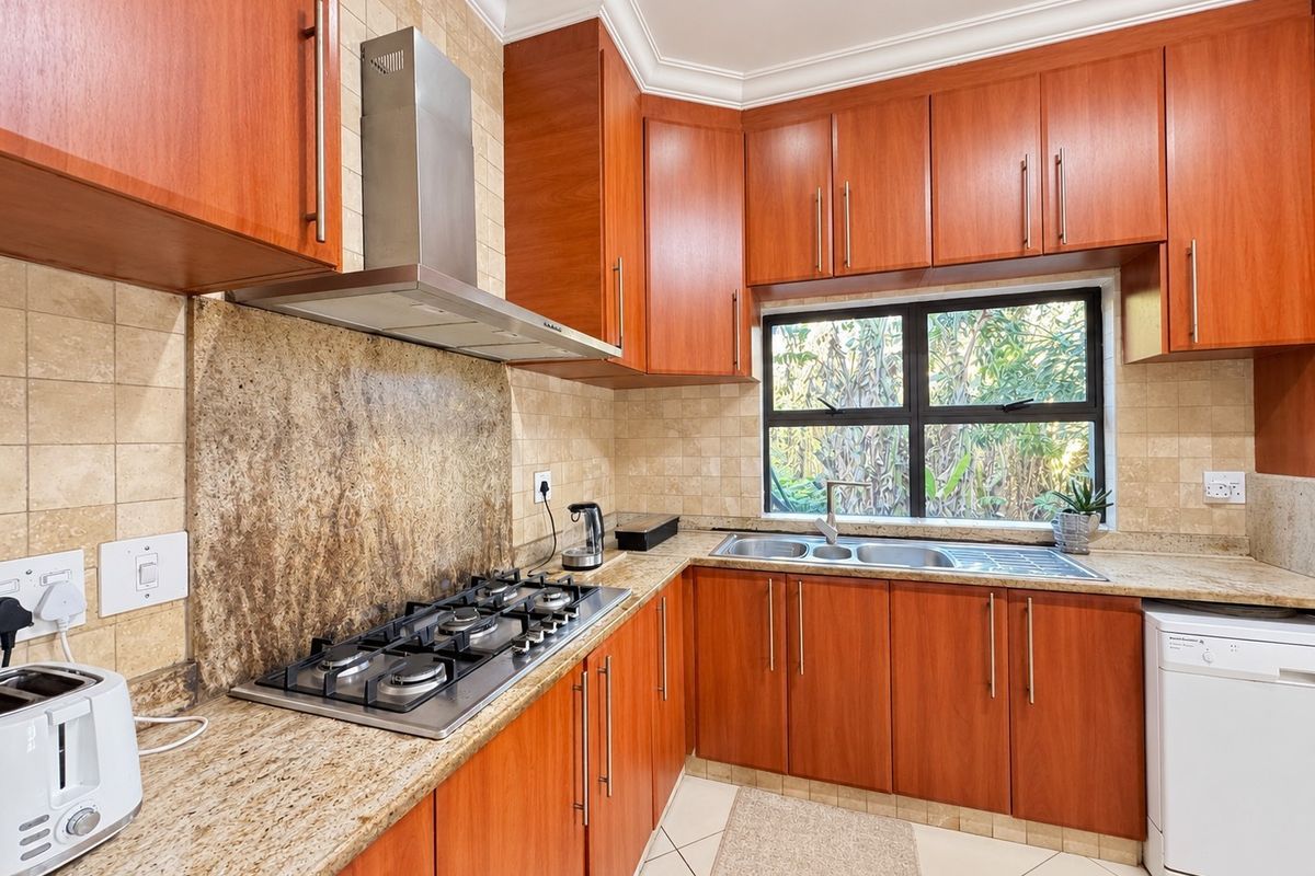A functional kitchen featuring warm-toned wooden cabinetry, granite countertops, a gas hob with extractor fan, and tiled finishes throughout.