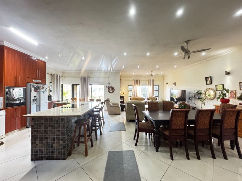 Spacious open-plan living area featuring a large kitchen island with granite countertops, tiled flooring, and recessed lighting throughout the combined kitchen and dining space.