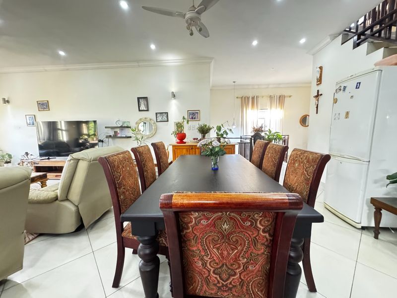 Spacious open-plan living and dining area featuring tiled flooring, recessed lighting, and a central staircase leading to the upper level.