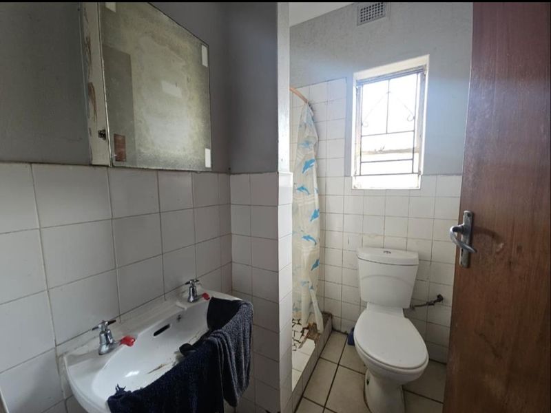 A dated bathroom featuring a pedestal basin, toilet, and shower area with tiled walls and floors, requiring cosmetic updates and renovation.
