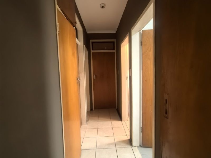 A narrow interior hallway featuring tiled flooring and multiple wooden doors leading to adjacent rooms.