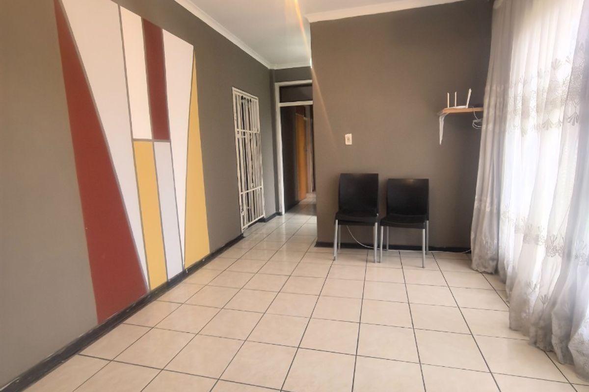 A spacious, tiled living area featuring neutral wall tones, a decorative accent wall, and a security gate leading to the hallway.