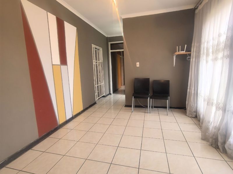 A spacious, tiled living area featuring neutral wall tones, a decorative accent wall, and a security gate leading to the hallway.