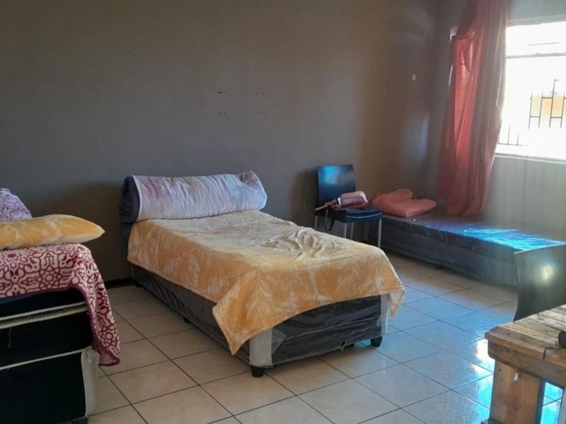 A bedroom featuring tiled flooring and a window with security bars, requiring cosmetic updates to the wall finishes.