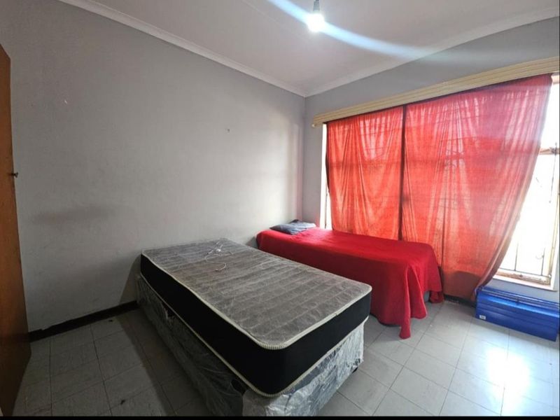 A bedroom featuring tiled flooring, cove cornicing, and security bars on the window, requiring cosmetic updates to improve its overall condition.