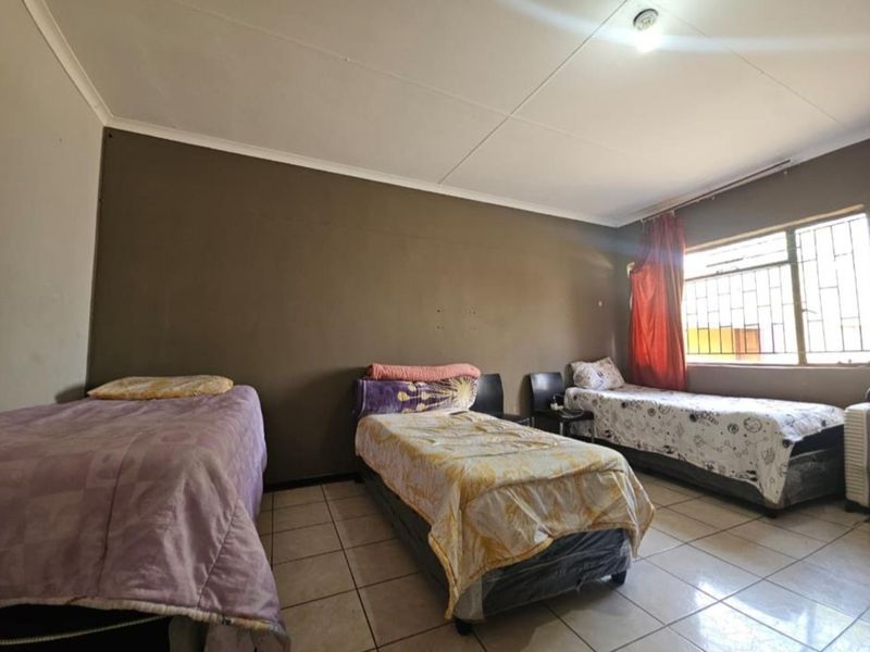 A spacious bedroom featuring tiled flooring, a large window with security bars, and neutral wall finishes.