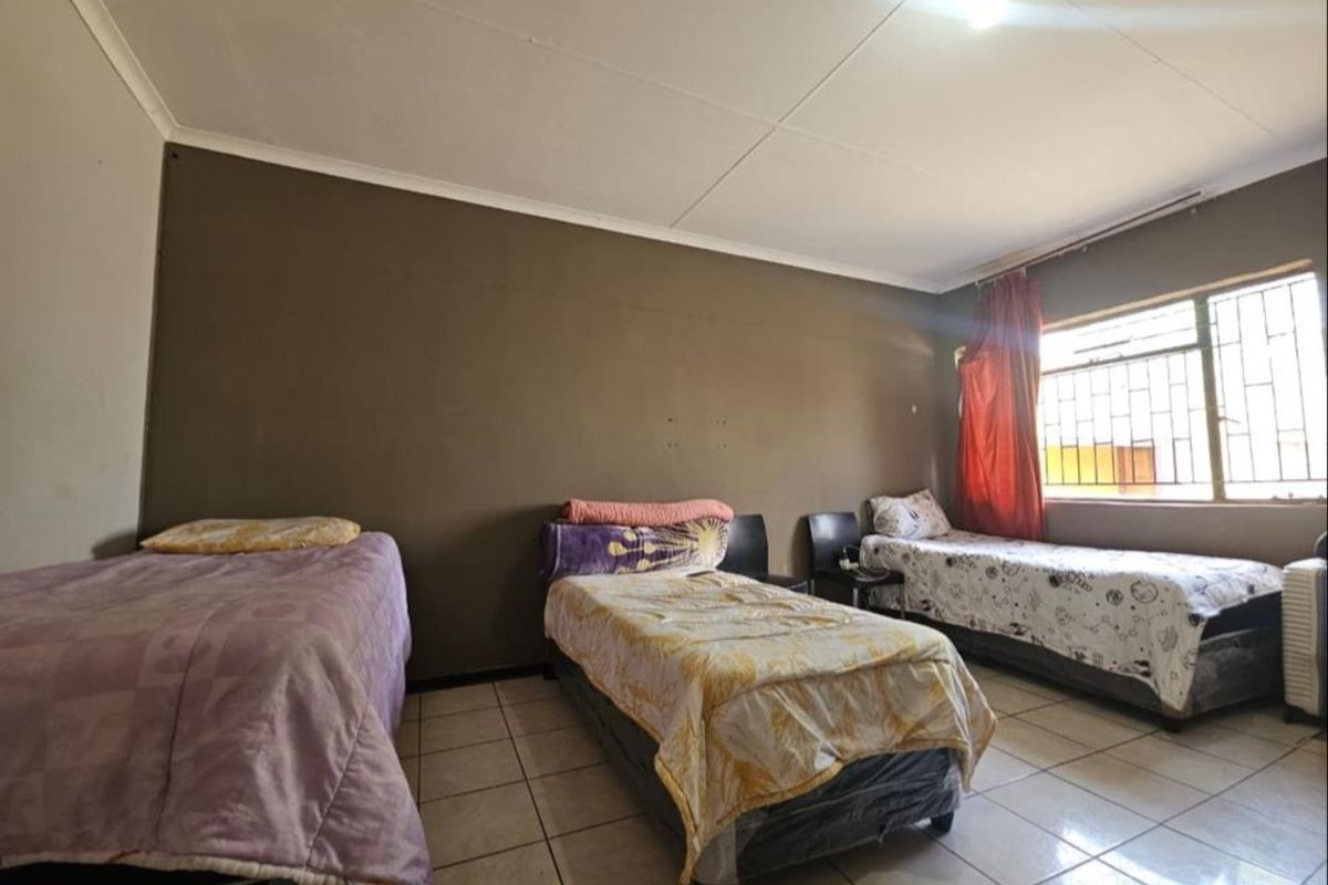 A spacious bedroom featuring tiled flooring, a large window with security bars, and neutral wall finishes.