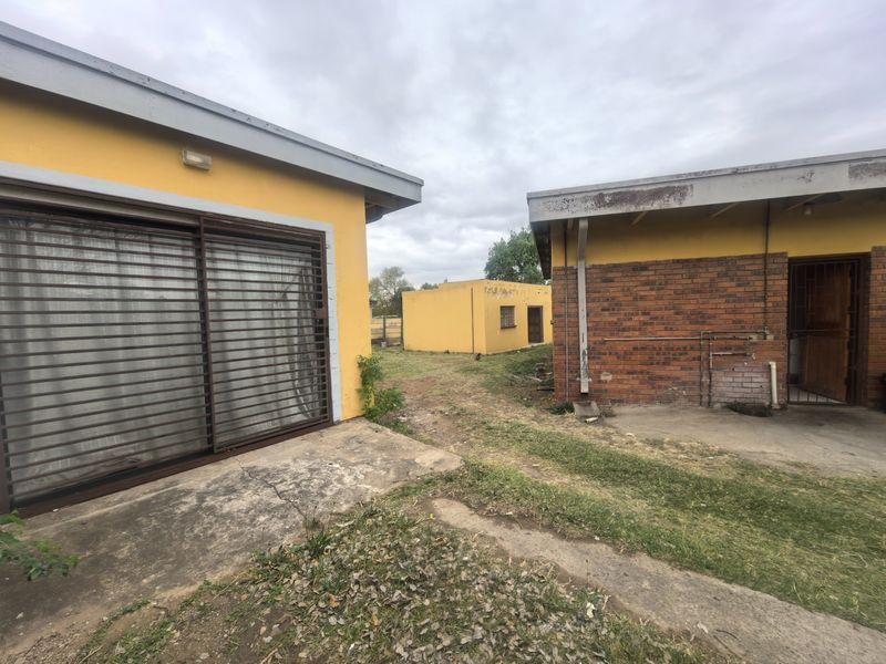 Rear view of the property showing multiple outbuildings, concrete patio areas, and brick and plastered wall finishes requiring maintenance.