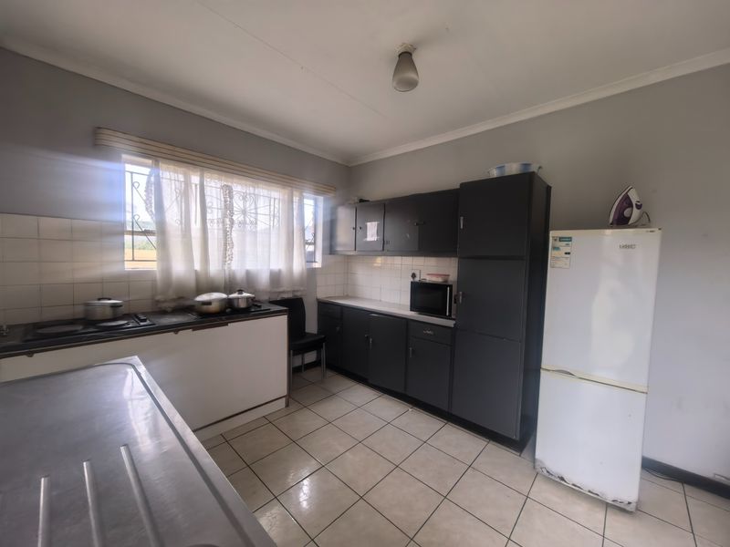 A functional kitchen featuring dark built-in cabinetry, tiled flooring, a tiled splashback, and a built-in hob, with security bars on the window.