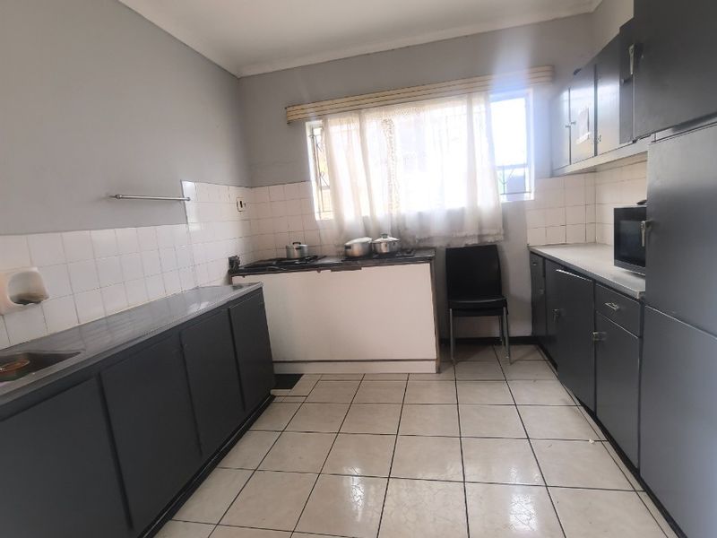 A functional kitchen featuring dark built-in cabinetry, tiled splashbacks, and tiled flooring, offering a practical layout with potential for modern updates.