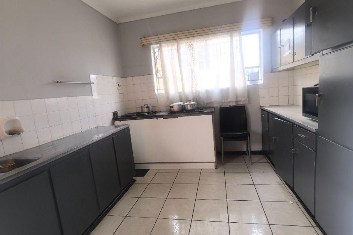 A functional kitchen featuring dark built-in cabinetry, tiled splashbacks, and tiled flooring, offering a practical layout with potential for modern updates.