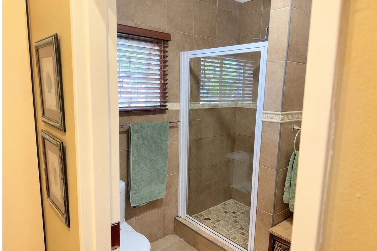 A functional bathroom featuring a tiled shower enclosure, toilet, and neutral wall tiling, viewed through a doorway.