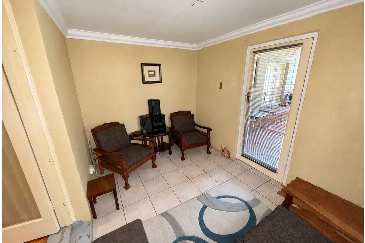 A living area featuring tiled flooring, cornicing, and a glass panel door leading to an outdoor space, requiring minor cosmetic repairs.