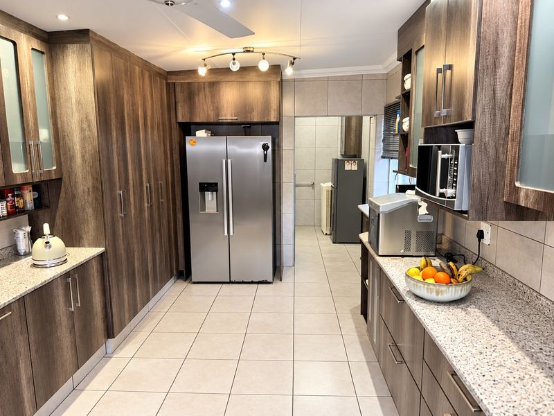 A well-maintained kitchen featuring modern wood-finish cabinetry, granite countertops, tiled flooring, and a built-in microwave, with an adjacent scullery area.