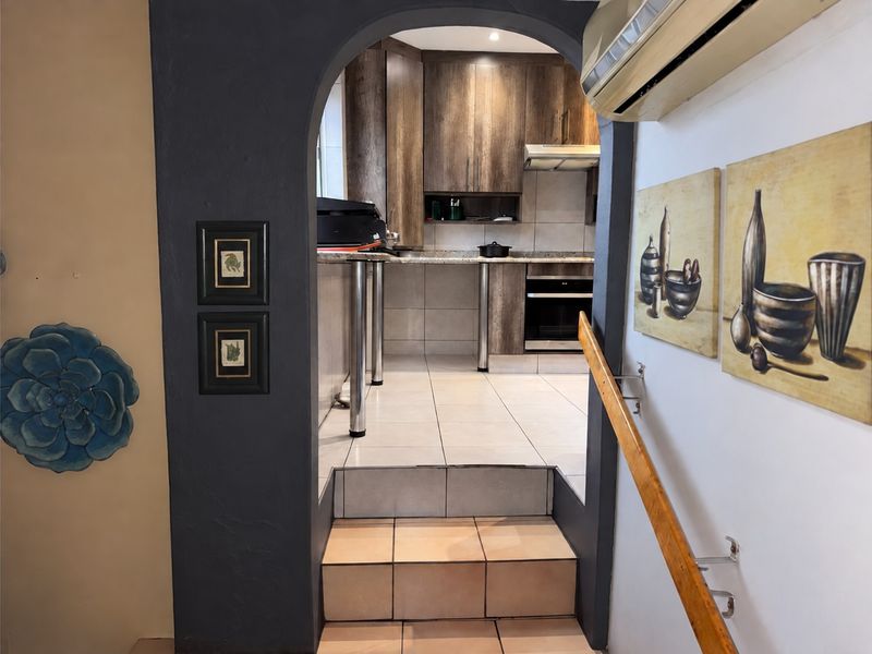 A view through an arched doorway into a functional kitchen featuring wood-finish cabinetry, granite countertops, built-in oven, and tiled flooring.