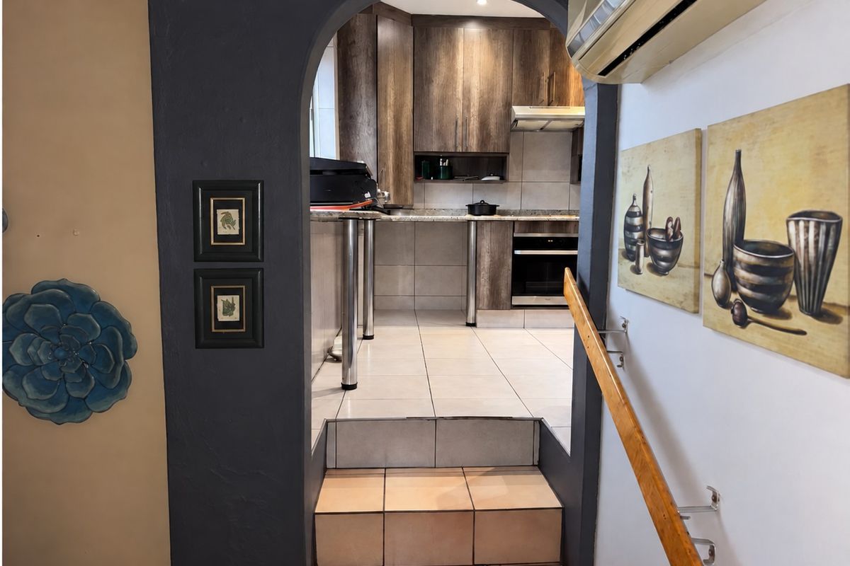 A view through an arched doorway into a functional kitchen featuring wood-finish cabinetry, granite countertops, built-in oven, and tiled flooring.