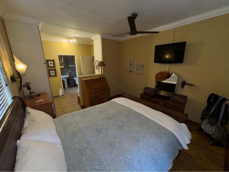 A bedroom featuring laminate flooring, a ceiling fan, and an open-plan en-suite bathroom with a pedestal basin.