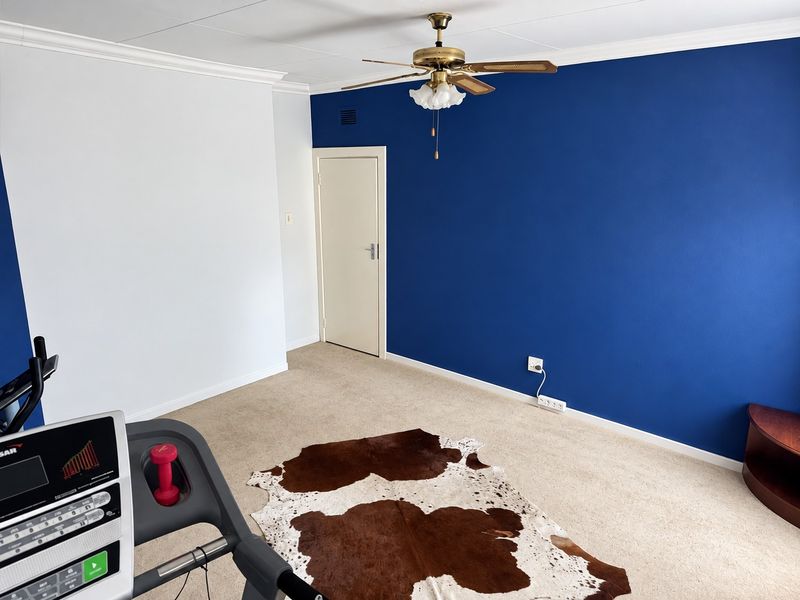 A bedroom featuring a ceiling fan, carpeted flooring, and a bold blue accent wall, offering a versatile space for rest or home activities.