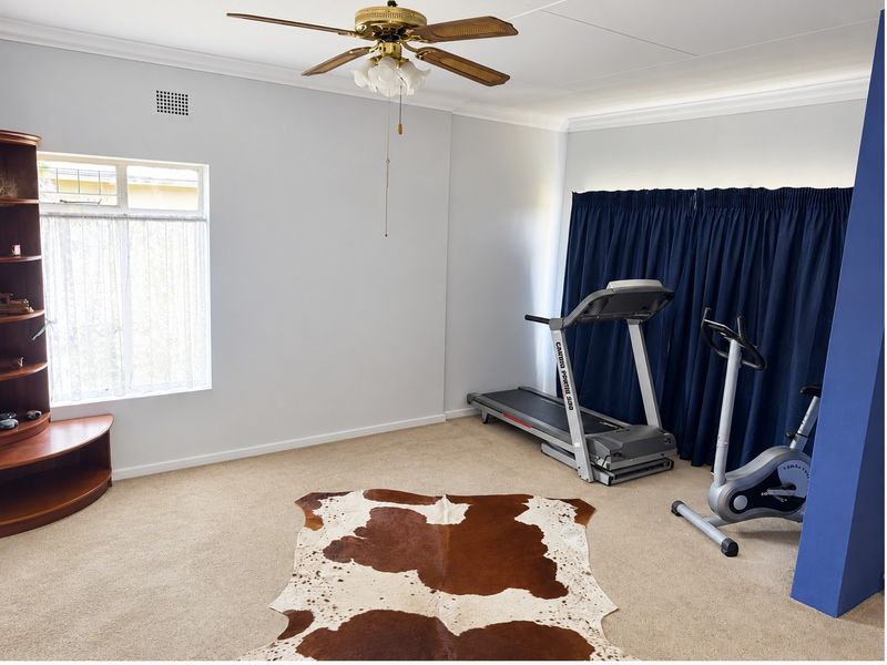 A functional home gym space featuring neutral carpeting, a ceiling fan, and a window with natural light.