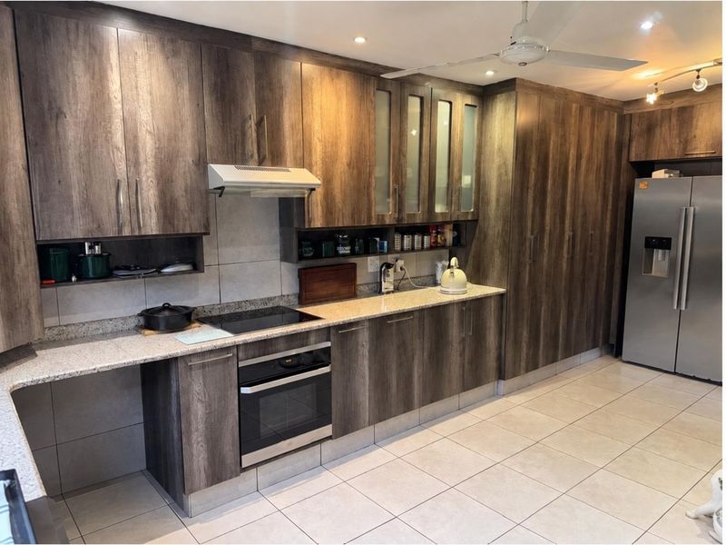 Modern kitchen featuring dark wood-grain cabinetry, granite countertops, integrated oven and hob, and neutral tiled flooring.