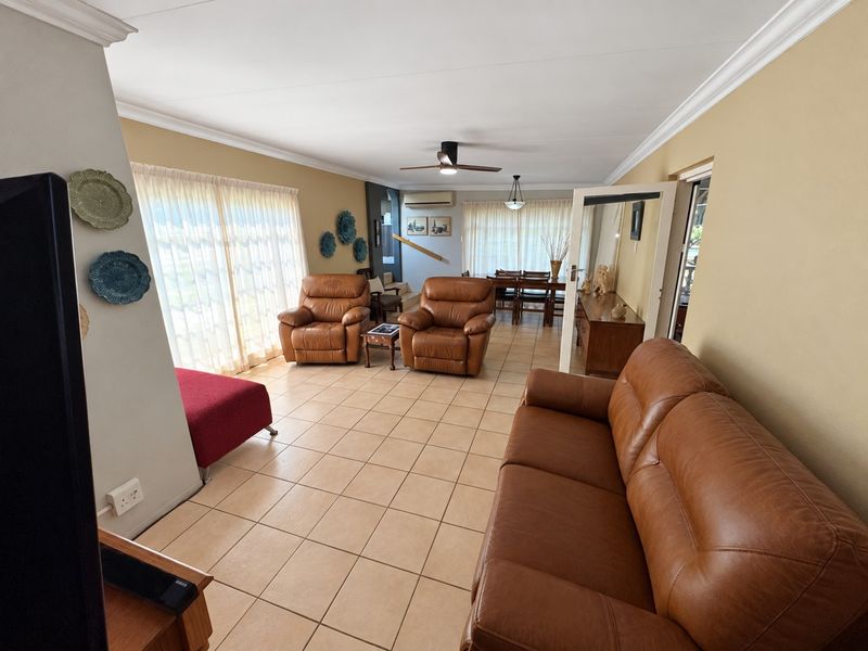 Spacious open-plan living and dining area featuring tiled flooring, crown molding, ceiling fan, air conditioning, and large sliding doors providing natural light.