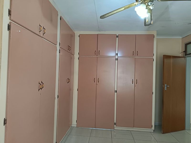 A bedroom featuring extensive built-in cupboards, tiled flooring, and a ceiling fan, offering a functional space with potential for modern updates.
