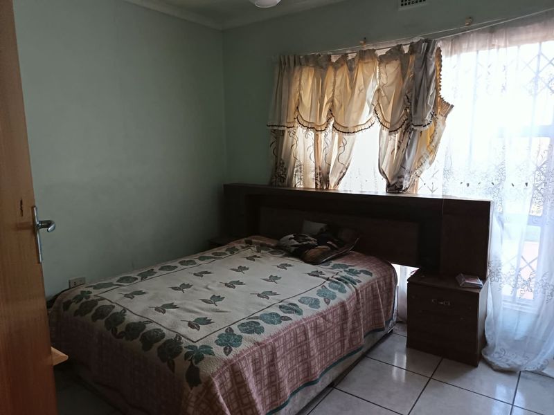A bedroom featuring tiled flooring, a built-in headboard, and a window with security bars, requiring cosmetic updates to improve its overall condition.