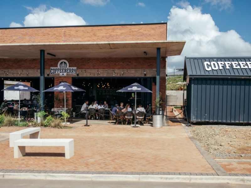 Modern commercial office or cafe building featuring an exposed brick facade, covered patio area, and adjacent metal container structure.