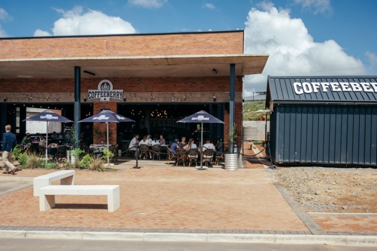 Modern commercial office or cafe building featuring an exposed brick facade, covered patio area, and adjacent metal container structure.